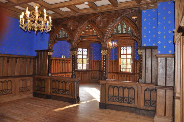 Neogotischer Innenraum von Schloss Wolfersdorf mit blauen Wänden, Holzvertäfelung und Kronleuchter